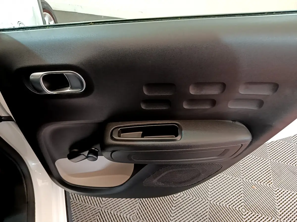 Vue rapprochée de la porte avant gauche blanche d'une Citroën C3 2018 avec poignée noire et haut-parleur intégré.