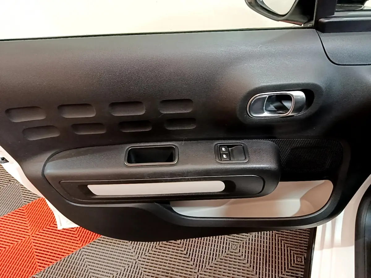 Gros plan sur la porte côté conducteur de la Citroën C3 blanche, montrant la poignée intérieure et les commandes de vitres électriques.