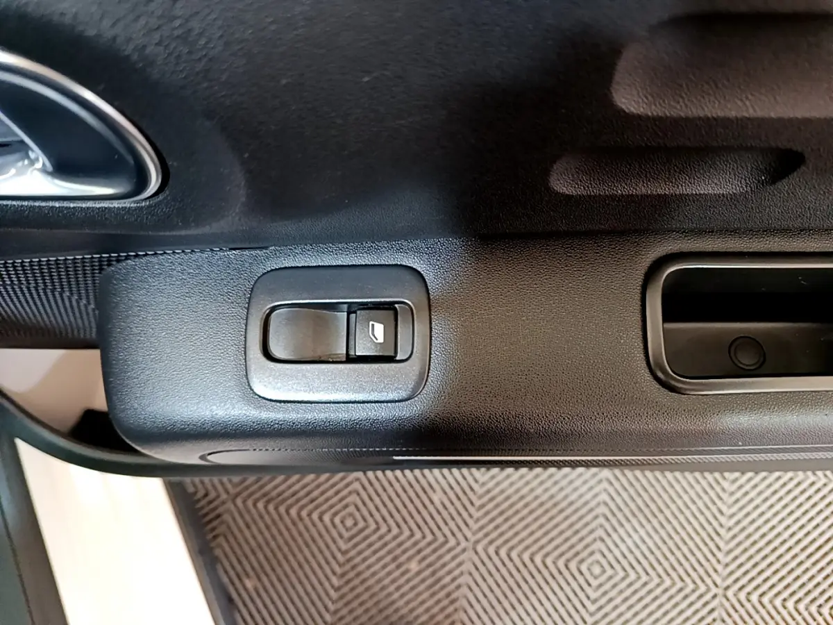 Gros plan sur la commande de lève-vitre côté conducteur de la porte intérieure noire d'une Citroën C3 blanche.