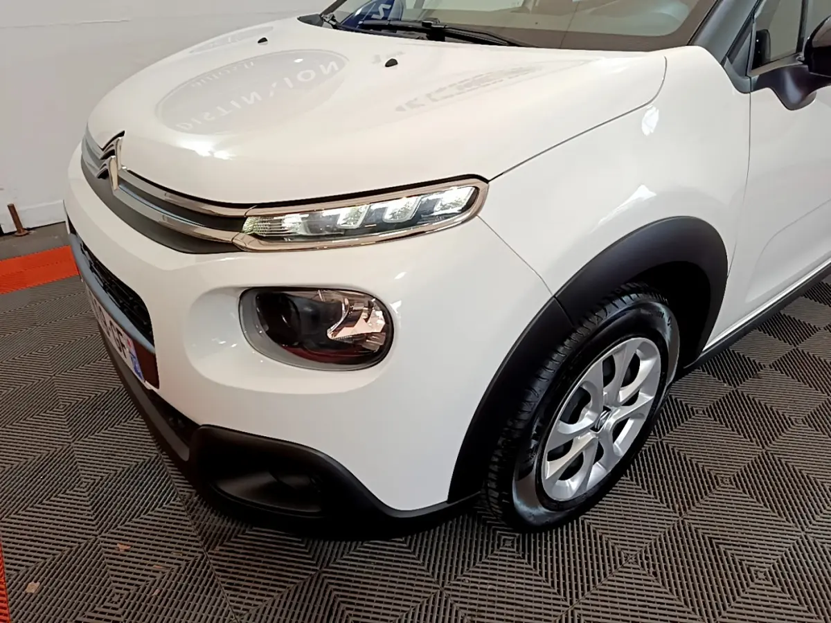 Vue 3/4 avant droit d'une Citroën C3 blanche mettant en valeur ses phares LED et ses protections noires contrastantes.