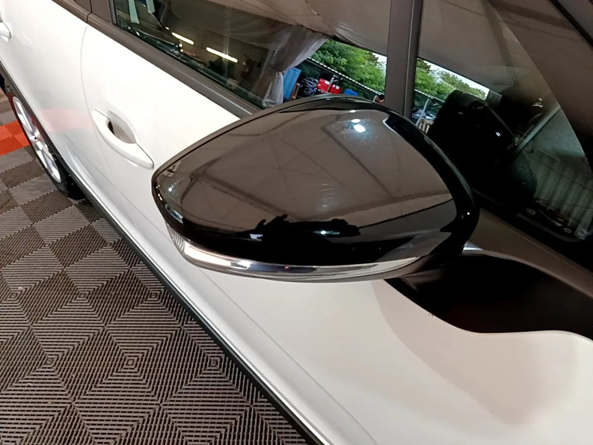 Gros plan sur le rétroviseur noir brillant côté gauche d'une Citroën C3 blanche, avec poignée de porte visible.