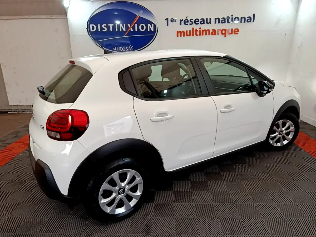 Citroën C3 blanc vue 3/4 arrière droit, avec jantes alliage et protections noires sur les passages de roues.