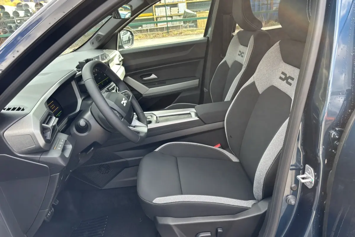 Intérieur avant droit du Dacia Bigster Hybrid 155 Journey Plus bleu indigo, sièges bi-ton gris et noir avec volant cuir.