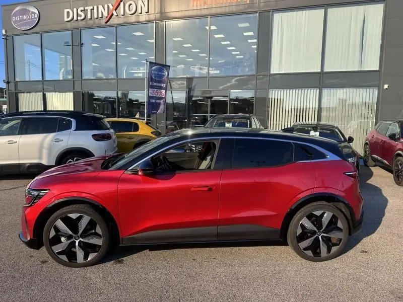 Profil côté gauche de la Renault Mégane E-Tech Electric rouge flamme 2023, avec jantes noires et toit argenté visible.