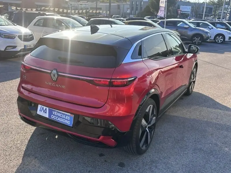 Vue 3/4 arrière droite d'une Renault Mégane E-Tech Electric rouge flamme 2023 avec toit noir et feux arrière LED continus.