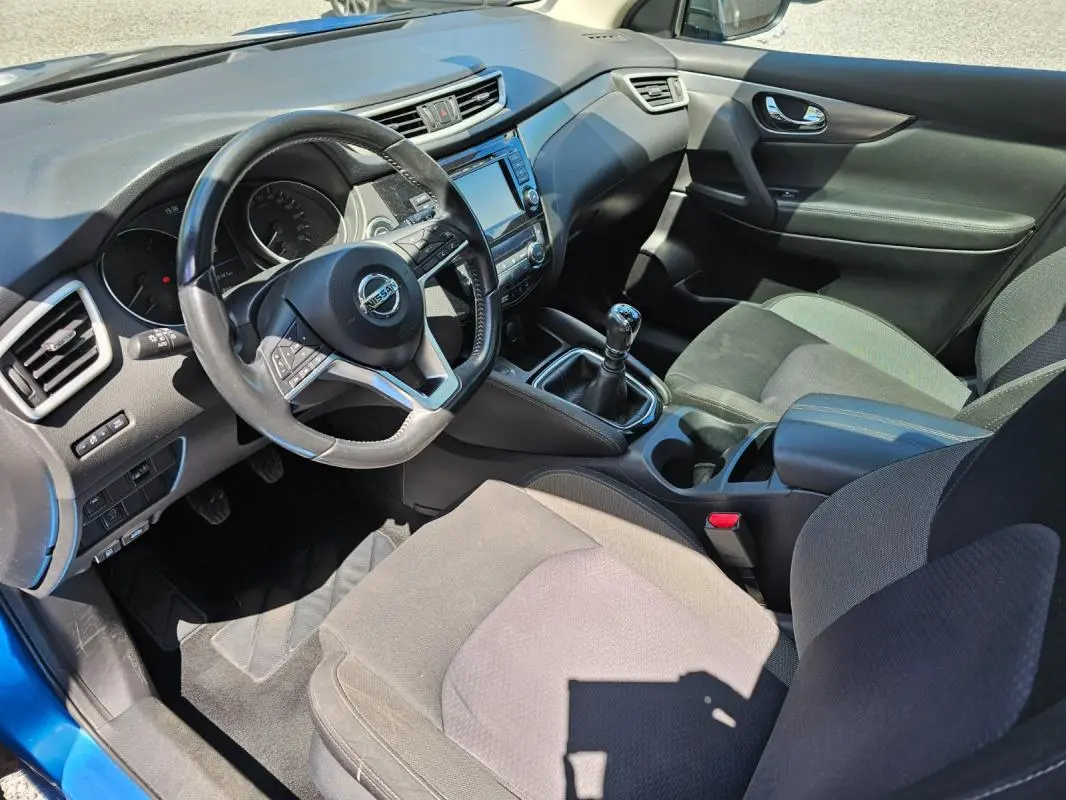 Vue intérieure côté conducteur du Nissan Qashqai bleu 2019, avec volant, tableau de bord et levier de vitesse manuel visibles.