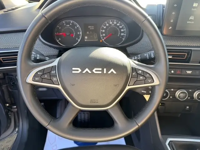 Vue rapprochée du volant en cuir synthétique noir d'une Dacia Sandero Stepway 2025, avec tableau de bord et commandes visibles.