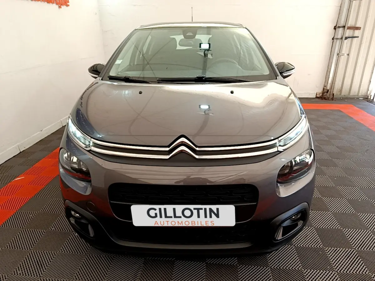 Vue frontale d'une Citroën C3 gris foncé 2019 avec phares LED et calandre chromée dans un showroom.