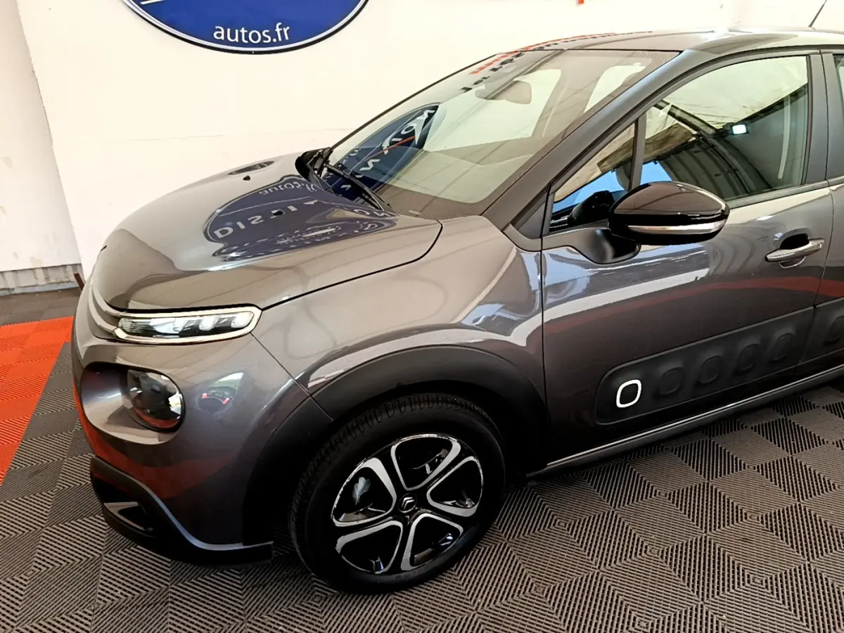Vue 3/4 avant droit d'une Citroën C3 gris foncé avec jantes noires et détails Airbump blancs sur la porte.
