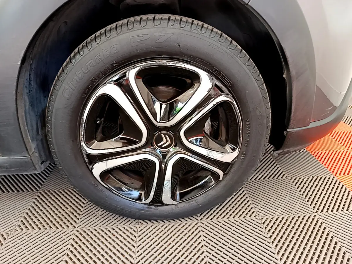 Gros plan sur la roue avant droite d'une Citroën C3 gris foncé, mettant en valeur la jante noire et chromée au design distinctif.