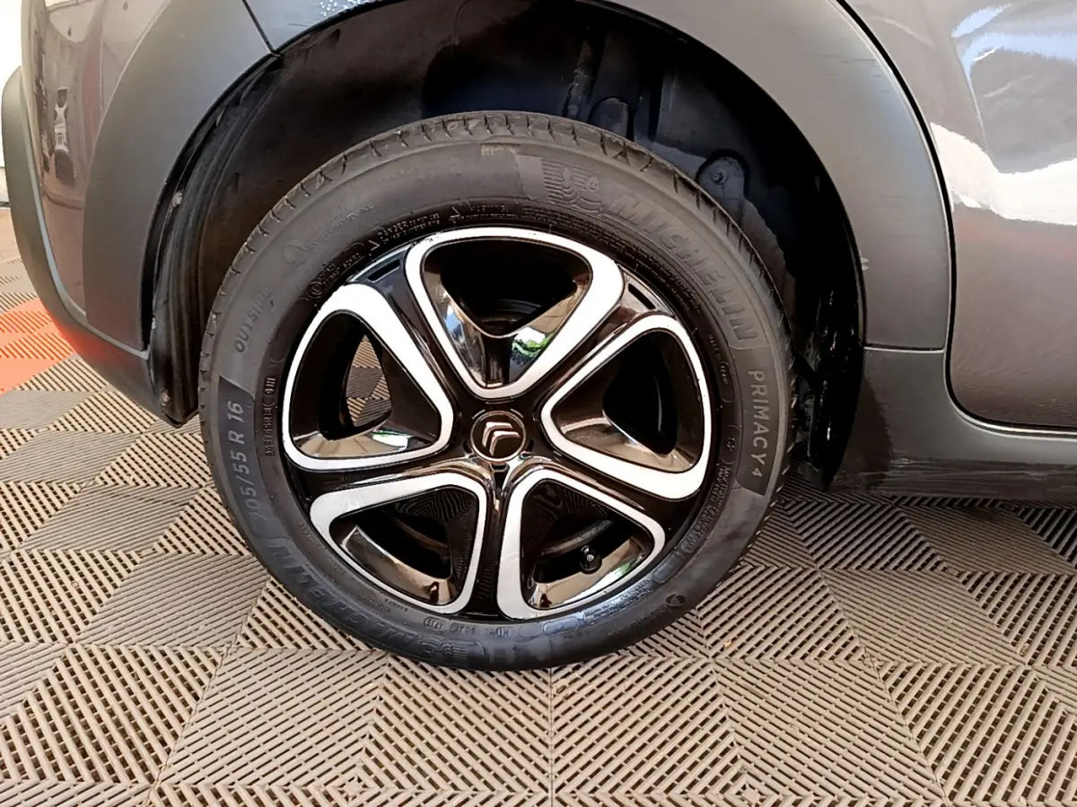 Gros plan sur la roue avant gauche de la Citroën C3 gris foncé, soulignant la jante noire et chromée au design moderne.