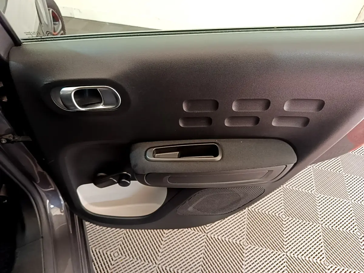 Porte intérieure côté gauche noire et grise de la Citroën C3 PureTech 82 Shine 2019 avec poignée et manivelle de vitre.