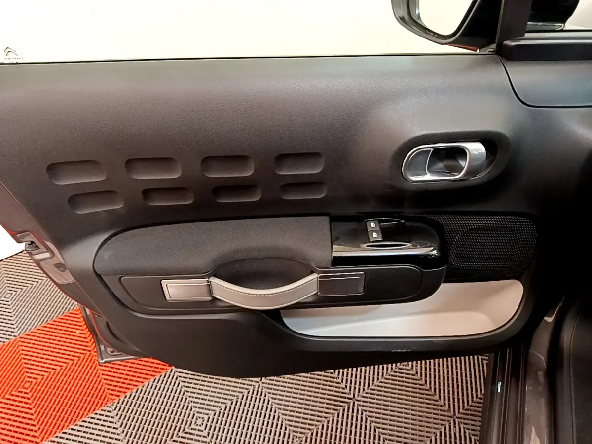 Vue intérieure côté gauche de la porte avant d'une Citroën C3 gris foncé avec poignée et commandes de vitres intégrées.