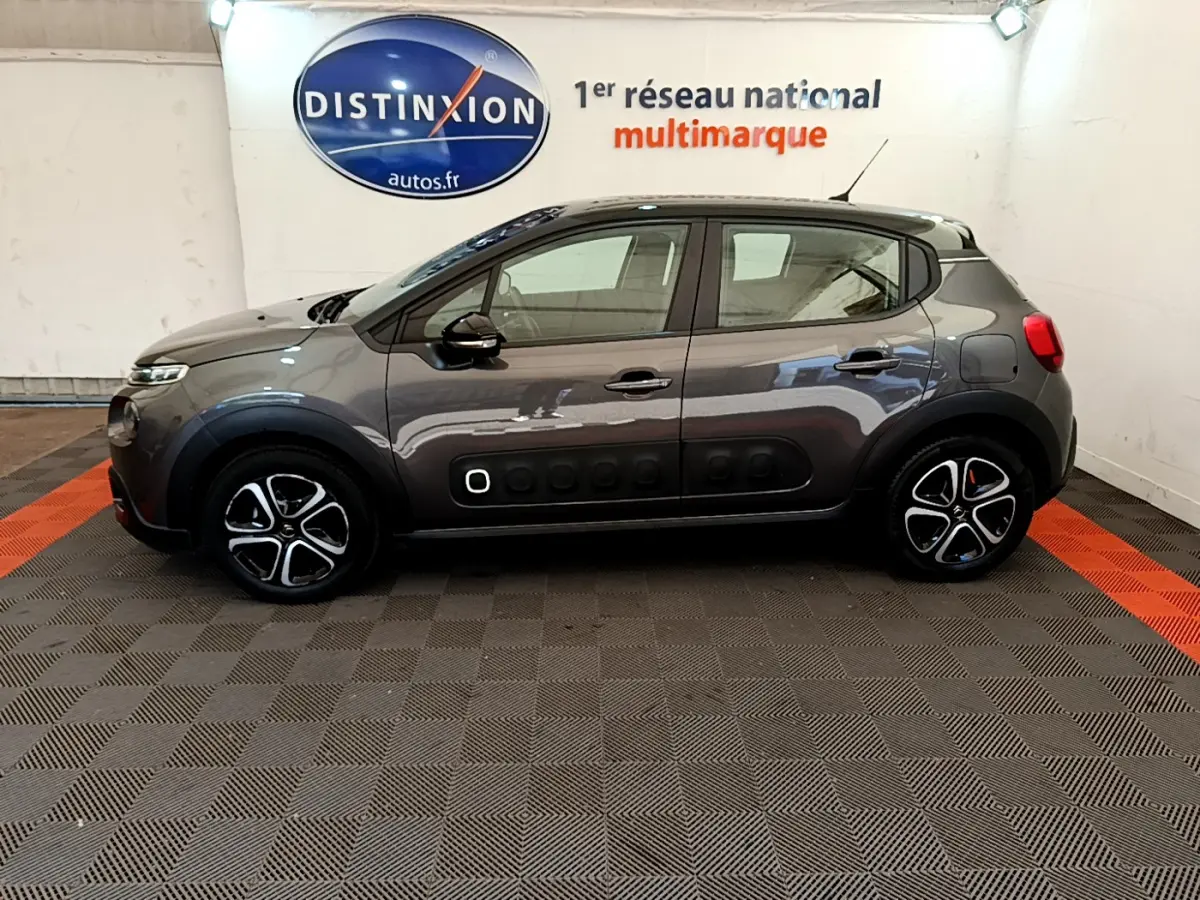 Profil côté gauche d'une Citroën C3 gris foncé 2019 avec protections latérales noires et jantes stylisées en intérieur showroom.