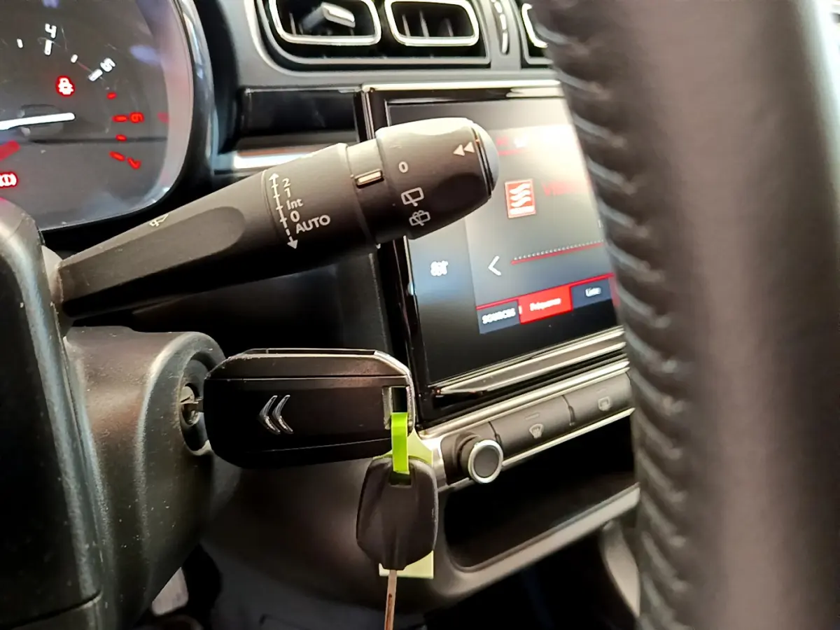 Gros plan intérieur sur la clé insérée et le commodo d'essuie-glace, avec écran tactile et volant cuir visibles.