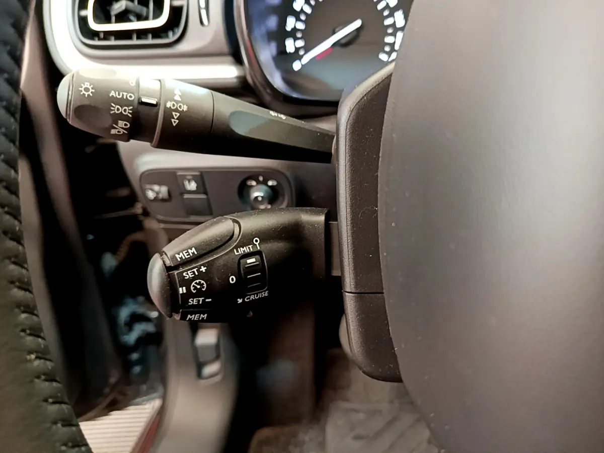 Gros plan sur la commande de régulateur de vitesse à gauche du volant cuir dans l'habitacle gris foncé d'une Citroën C3 2019.