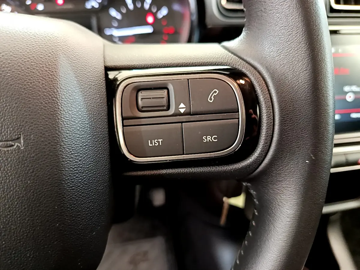 Gros plan sur les commandes gauche du volant cuir noir de la Citroën C3 Shine 2019, avec boutons multifonctions.