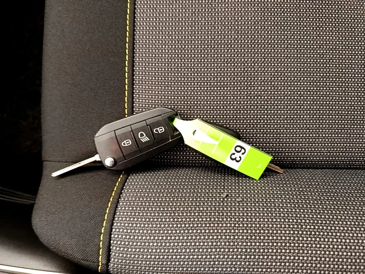 Clé de voiture noire posée sur un siège tissu gris foncé avec surpiqûres jaunes dans une Citroën C3.