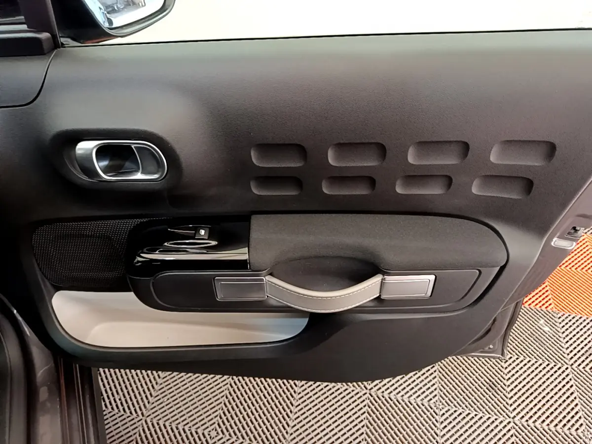 Vue intérieure côté gauche de la porte avant d'une Citroën C3 gris foncé avec poignée et commandes de vitre noires.