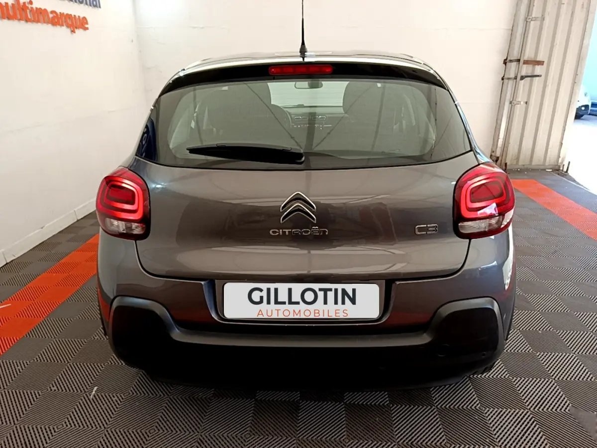 Vue arrière d'une Citroën C3 gris foncé avec feux arrière allumés dans un garage lumineux.