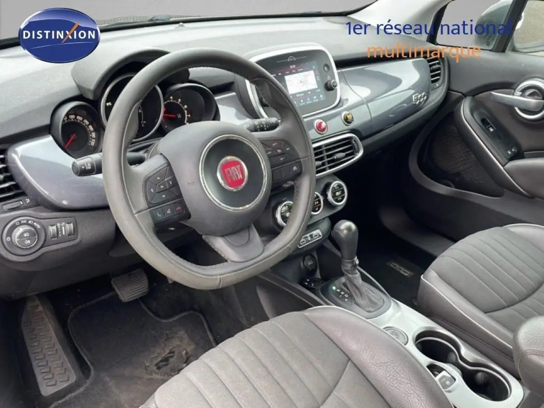 Vue intérieure côté conducteur du Fiat 500X gris foncé, montrant le volant, la console centrale et les sièges avant.