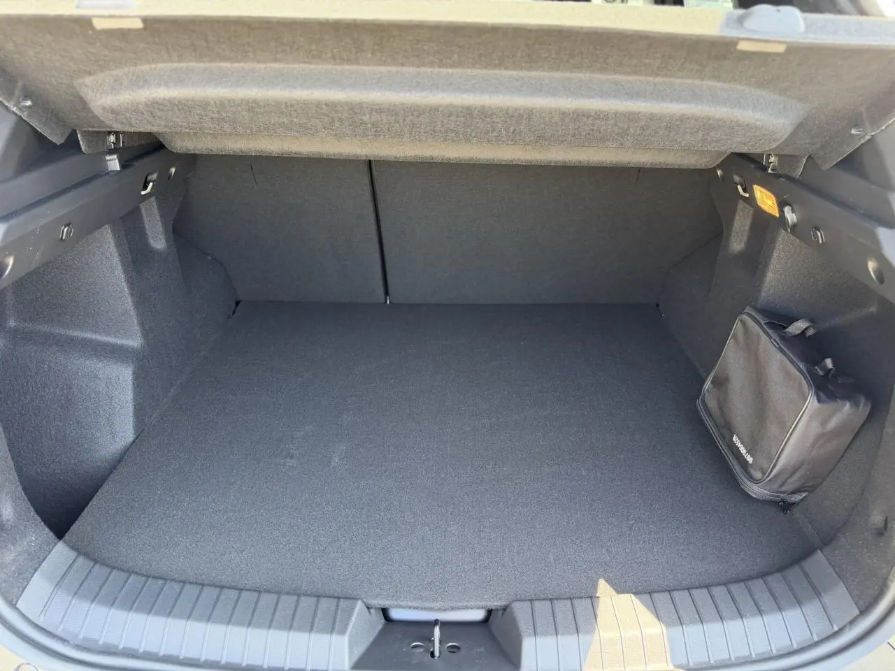 Coffre ouvert du Dacia Duster Hybrid-G 150 4X4 Journey 2026, vue intérieure avec tapis noir et trousse de secours fixée.