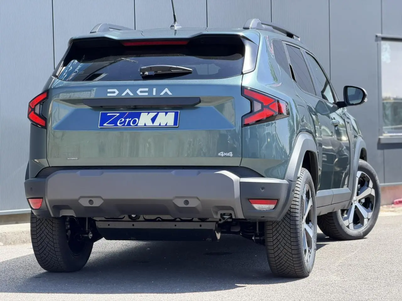 Vue 3/4 arrière droite du Dacia Duster Hybrid-G 150 4x4 en Vert Cèdre avec jantes alliage et barres de toit noires.