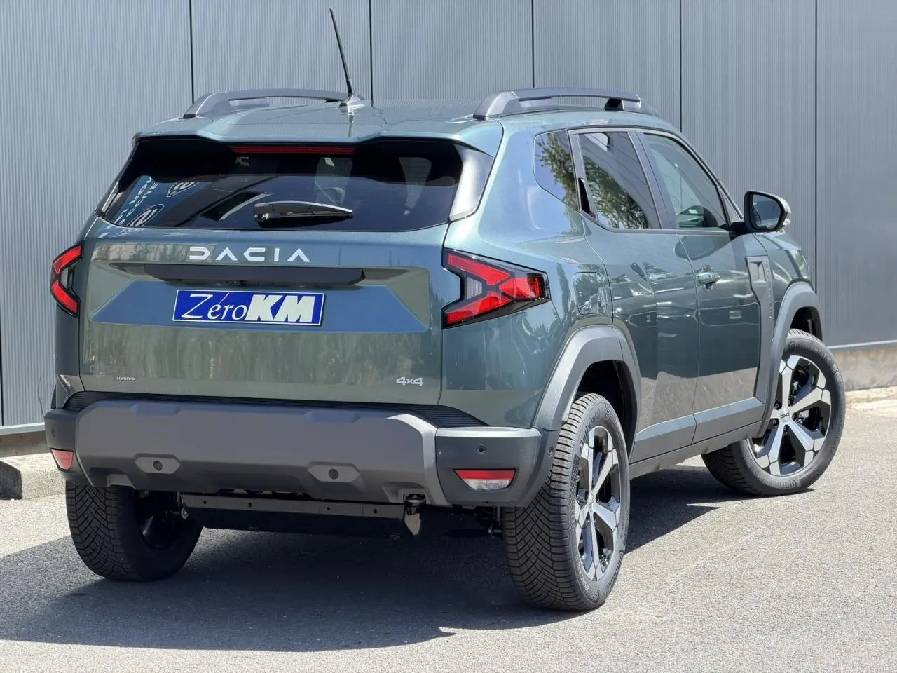 Vue 3/4 arrière droite du Dacia Duster 2026 Vert Cèdre avec barres de toit et jantes alliage 18 pouces.