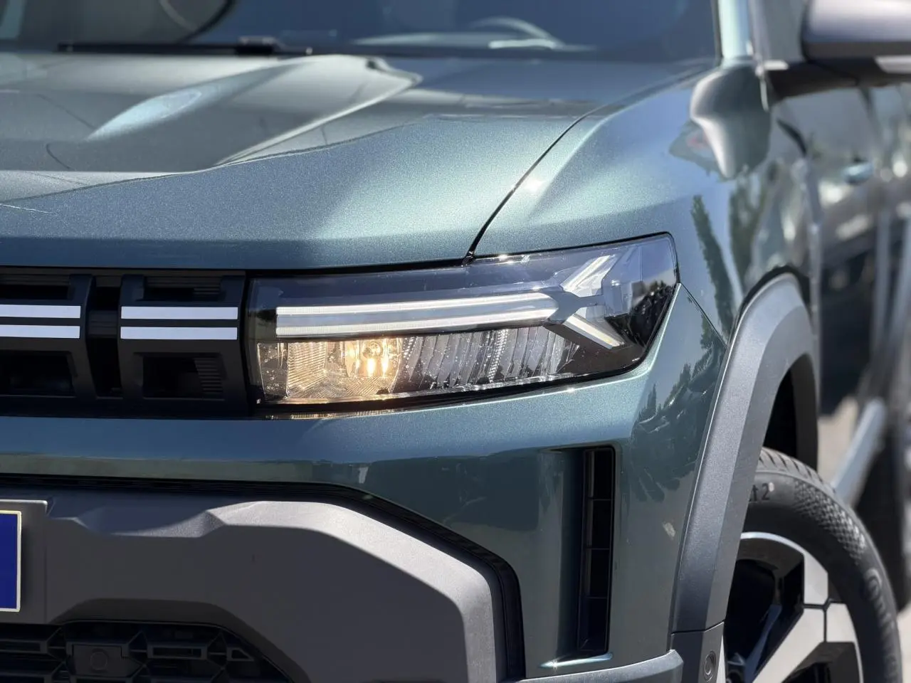 Gros plan sur l'avant droit du Dacia Duster Vert Cèdre 2026, mettant en valeur le phare LED et la calandre noire.