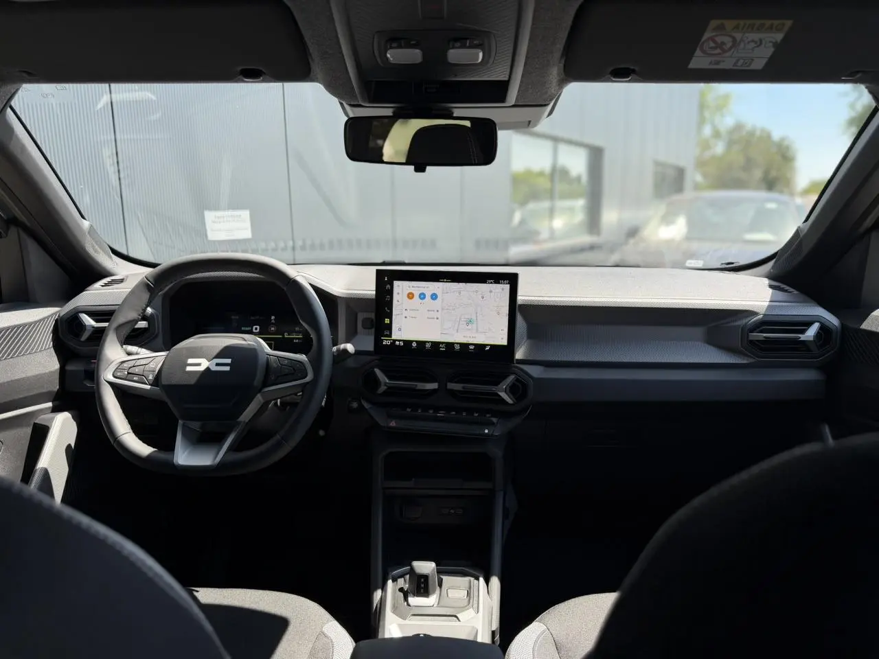 Vue intérieure frontale du tableau de bord du Dacia Duster 2026, avec écran tactile central et volant multifonction noir.