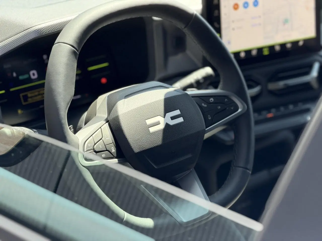 Gros plan sur le volant noir du Dacia Duster Hybrid-G 150 4x4, avec tableau de bord digital en arrière-plan.