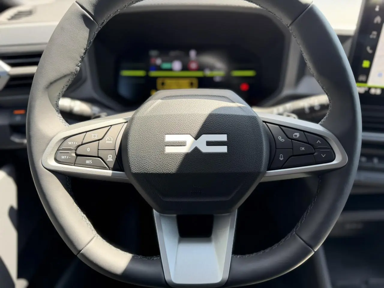 Vue rapprochée du volant noir du Dacia Duster Hybrid-G 150 4x4 avec commandes intégrées et tableau de bord digital flou.