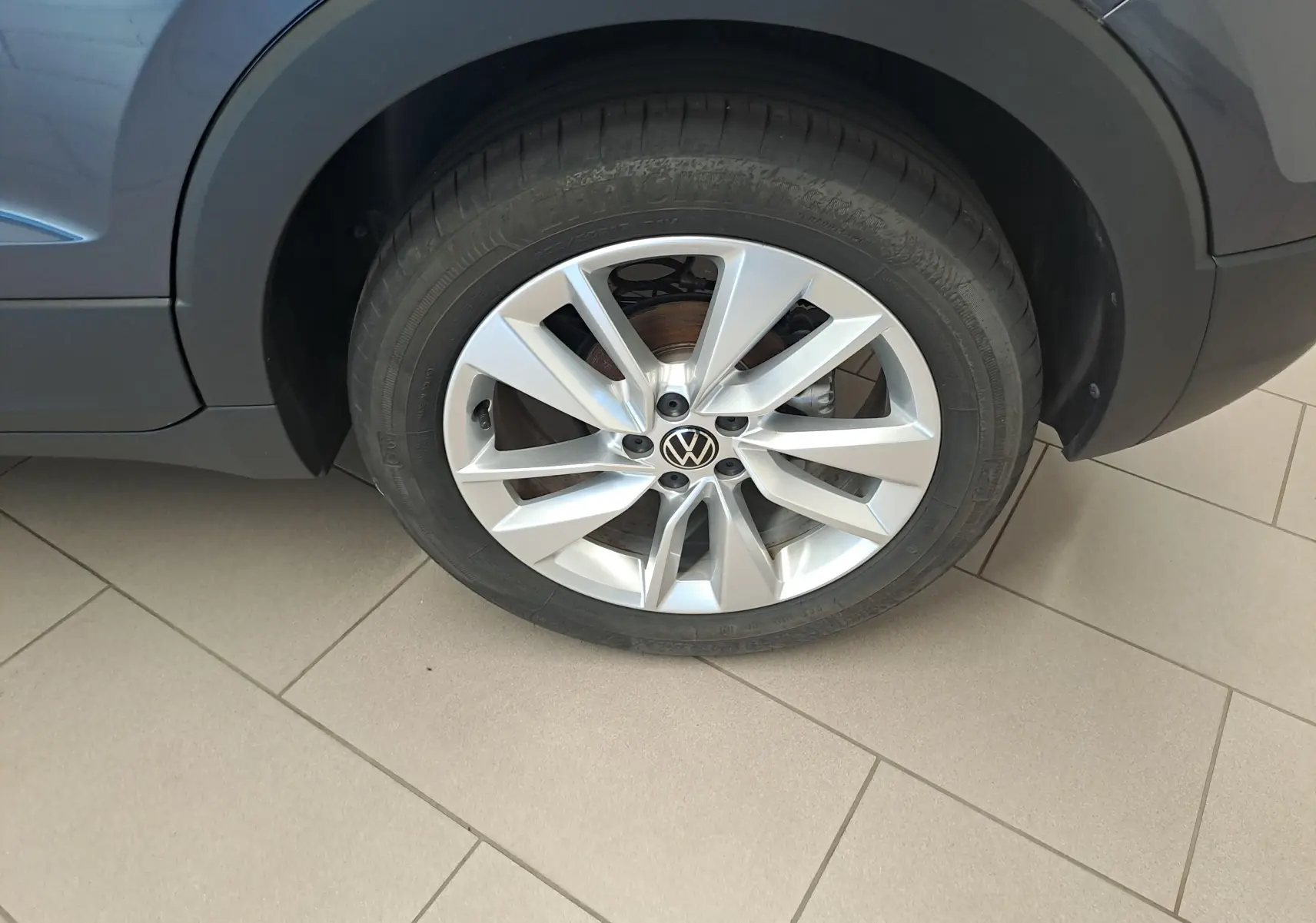 Gros plan sur la roue avant droite du Volkswagen T-Cross gris cendré, mettant en valeur la jante alliage à cinq branches doubles.