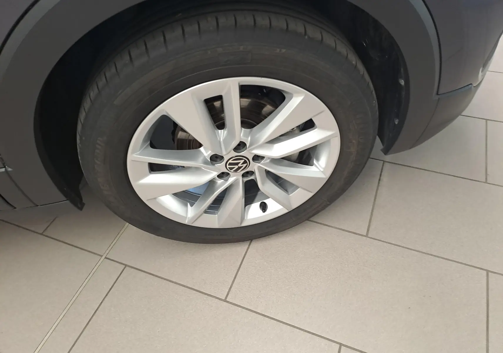 Gros plan sur la roue avant droite du Volkswagen T-Cross gris cendré, avec jante alliage à cinq doubles branches.