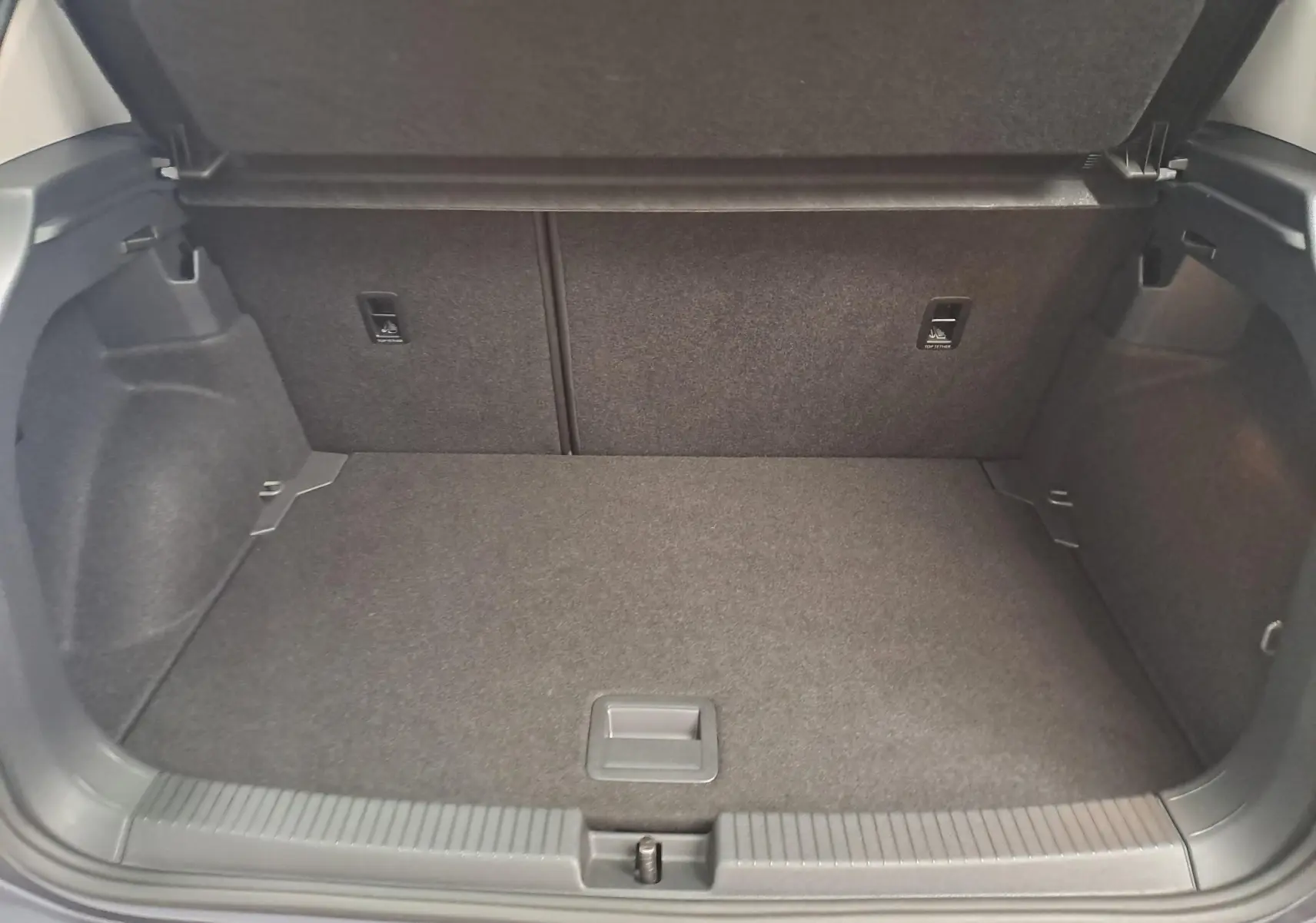 Coffre ouvert vu de l'arrière d'un Volkswagen T-Cross 2025 gris cendré, montrant l'espace de chargement vide et tapis gris.