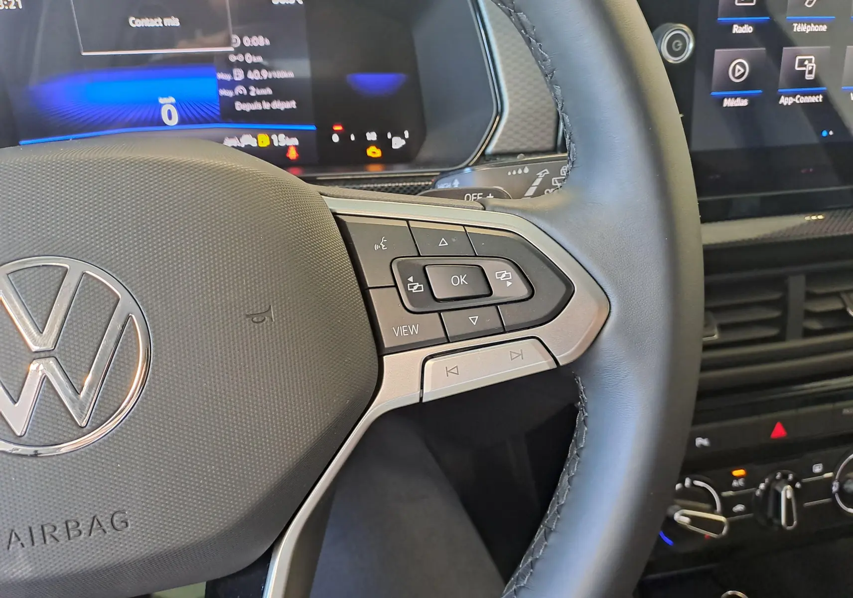 Gros plan sur le volant côté droit du Volkswagen T-Cross 2025 gris cendré, avec commandes multifonctions et tableau de bord numérique.