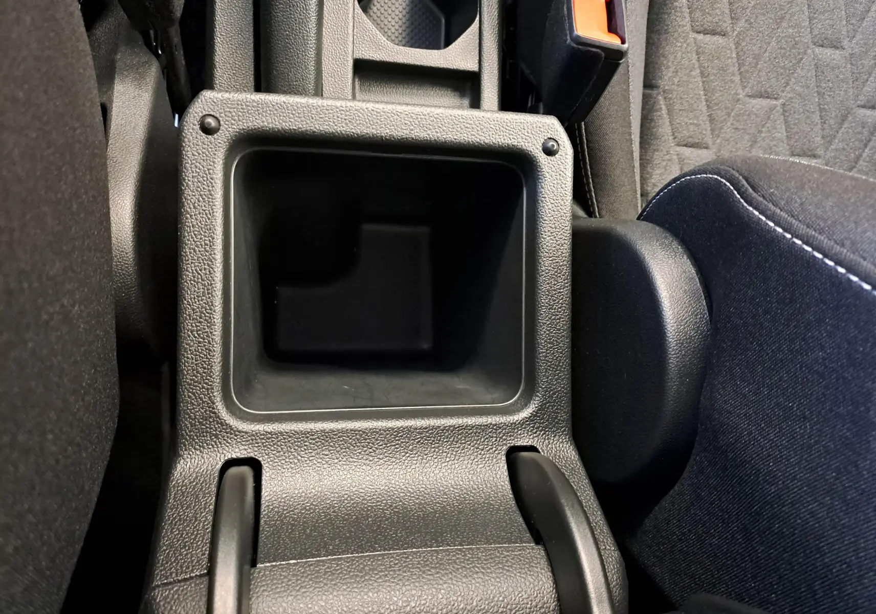 Gros plan sur le rangement central noir entre les sièges avant du Volkswagen T-Cross 2025, intérieur tissu gris.