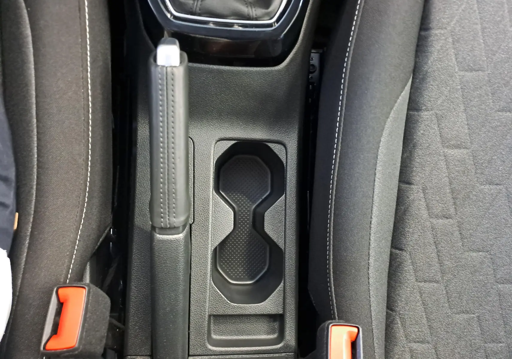 Vue plongeante sur la console centrale du Volkswagen T-Cross 2025, avec frein à main et porte-gobelets noirs.