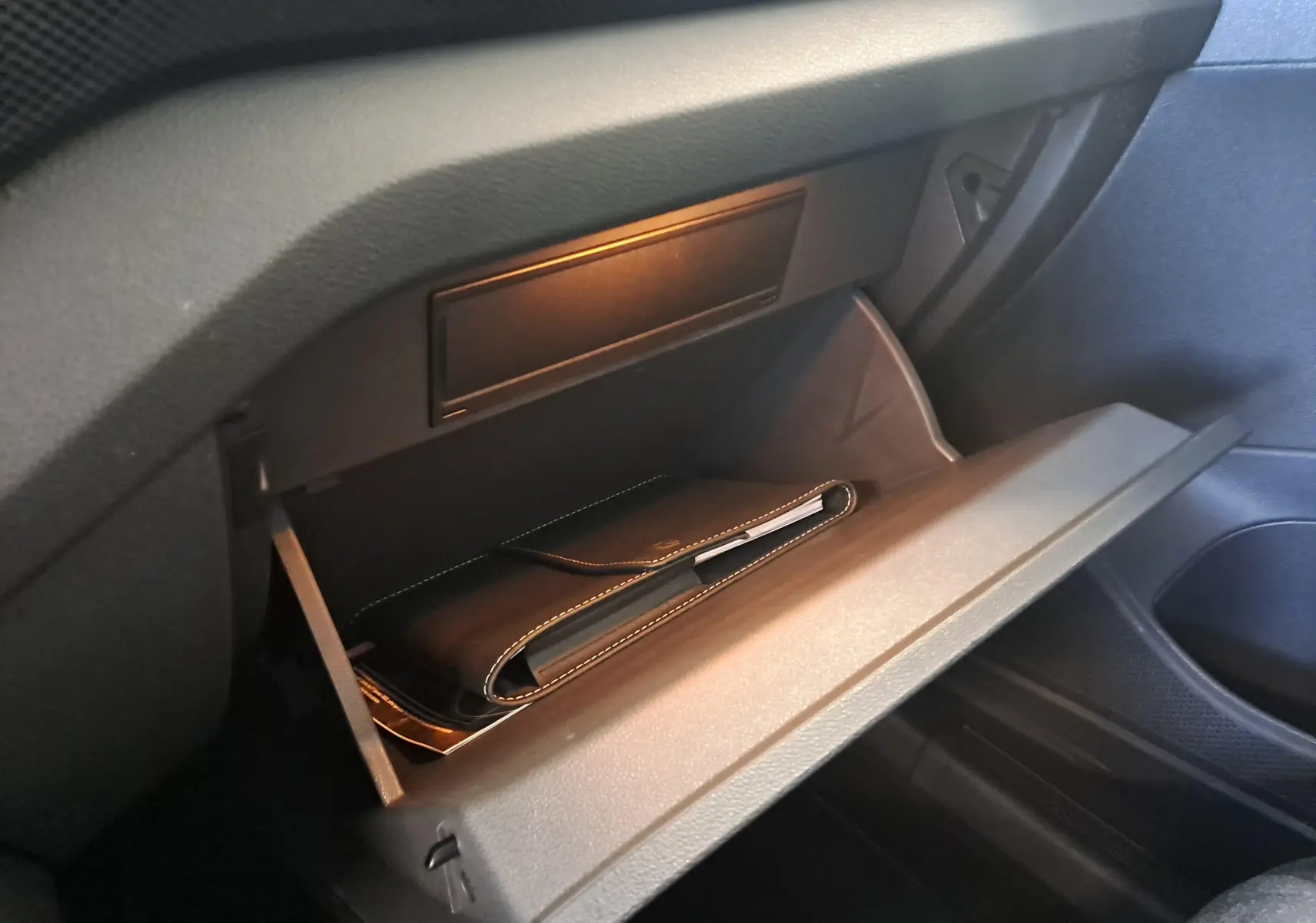Vue intérieure du Volkswagen T-Cross 2025, boîte à gants ouverte avec pochette noire visible, ambiance sobre et fonctionnelle.