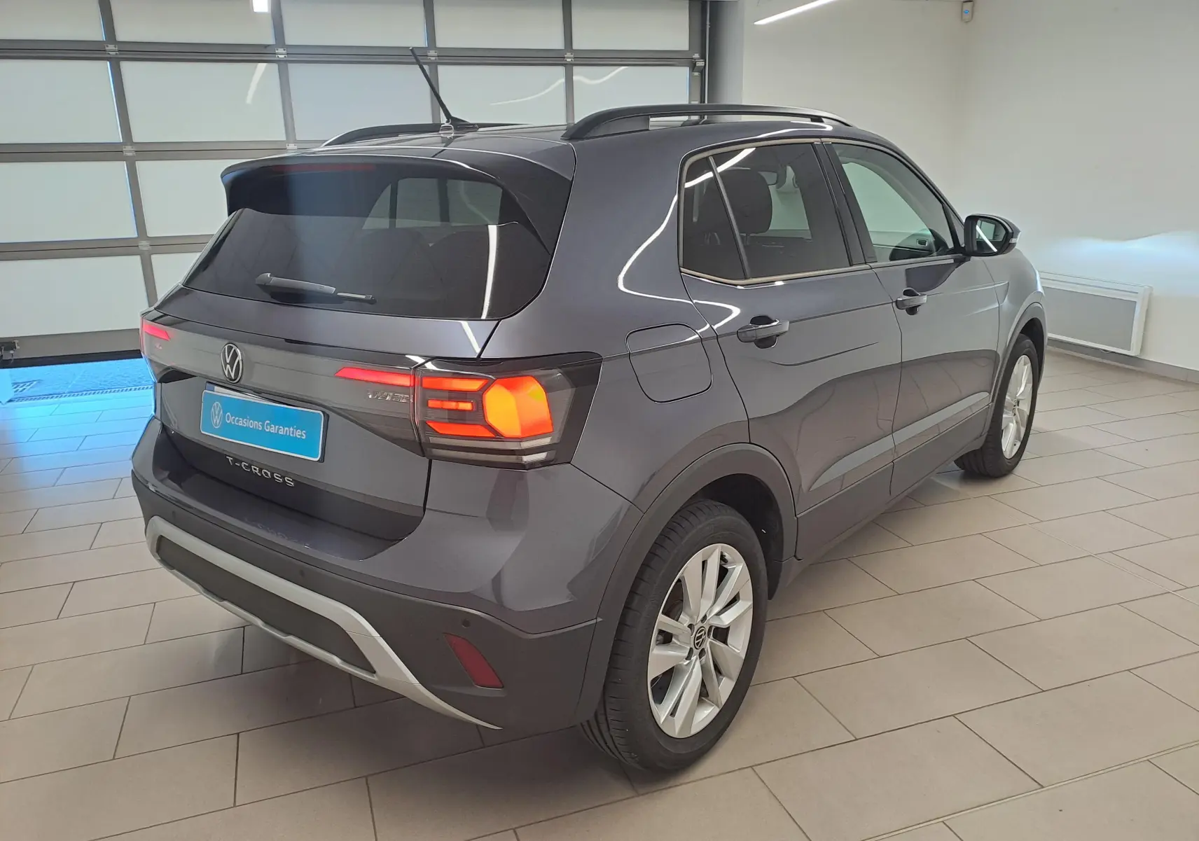Volkswagen T-Cross gris cendré en vue 3/4 arrière droit, avec feux arrière allumés et jantes alliage.