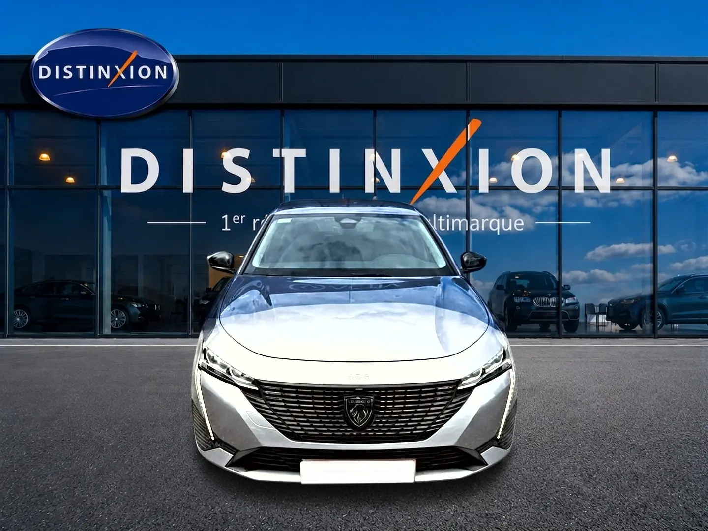 Vue frontale d'une Peugeot 308 SW gris métallisé avec calandre noire et phares LED, devant une vitrine Distinxion.