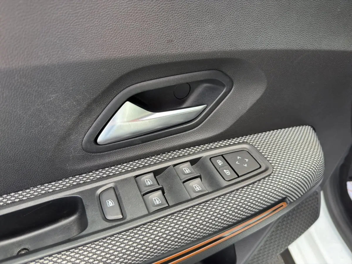 Gros plan sur la commande des vitres et poignée intérieure côté conducteur d'une Dacia Sandero Stepway blanche.