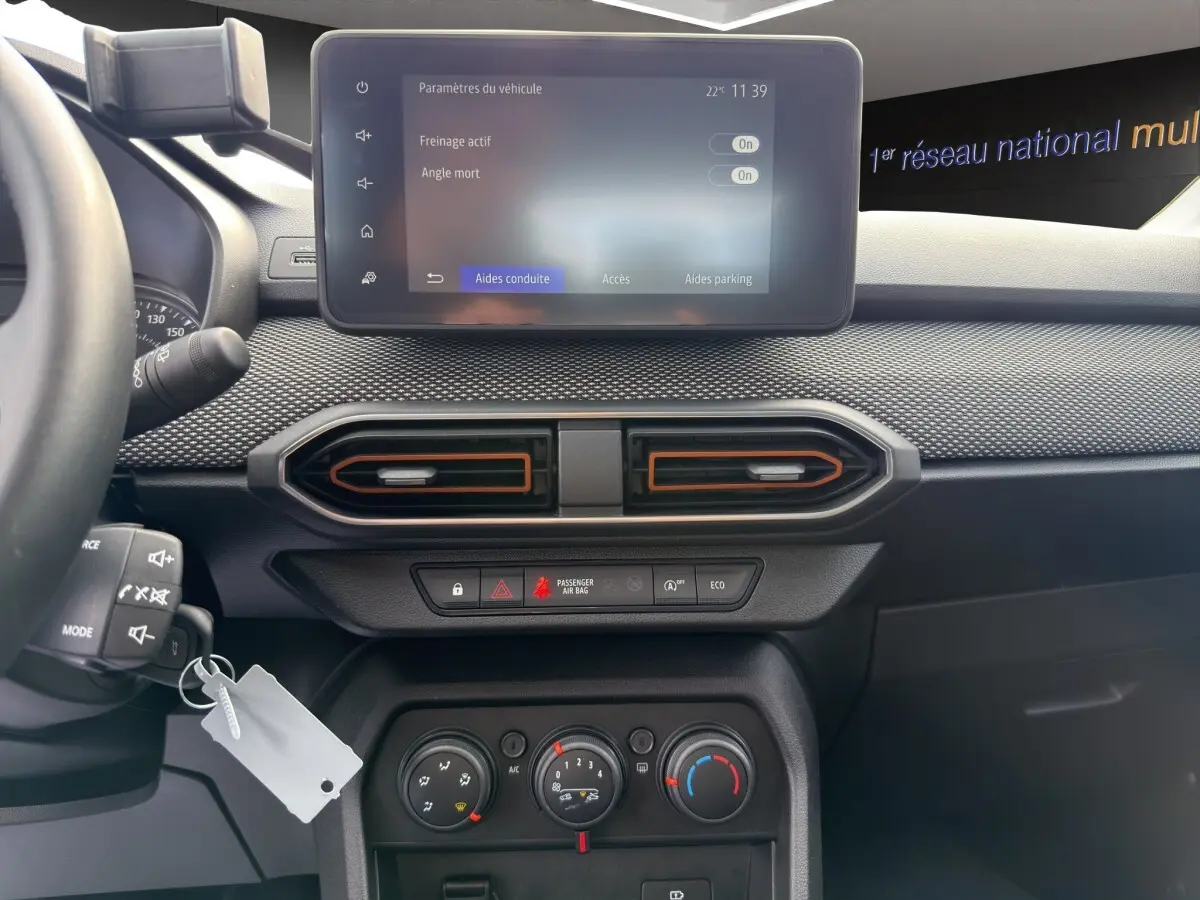 Vue intérieure du tableau de bord de la Dacia Sandero Stepway blanc, avec écran tactile central et aérateurs hexagonaux.