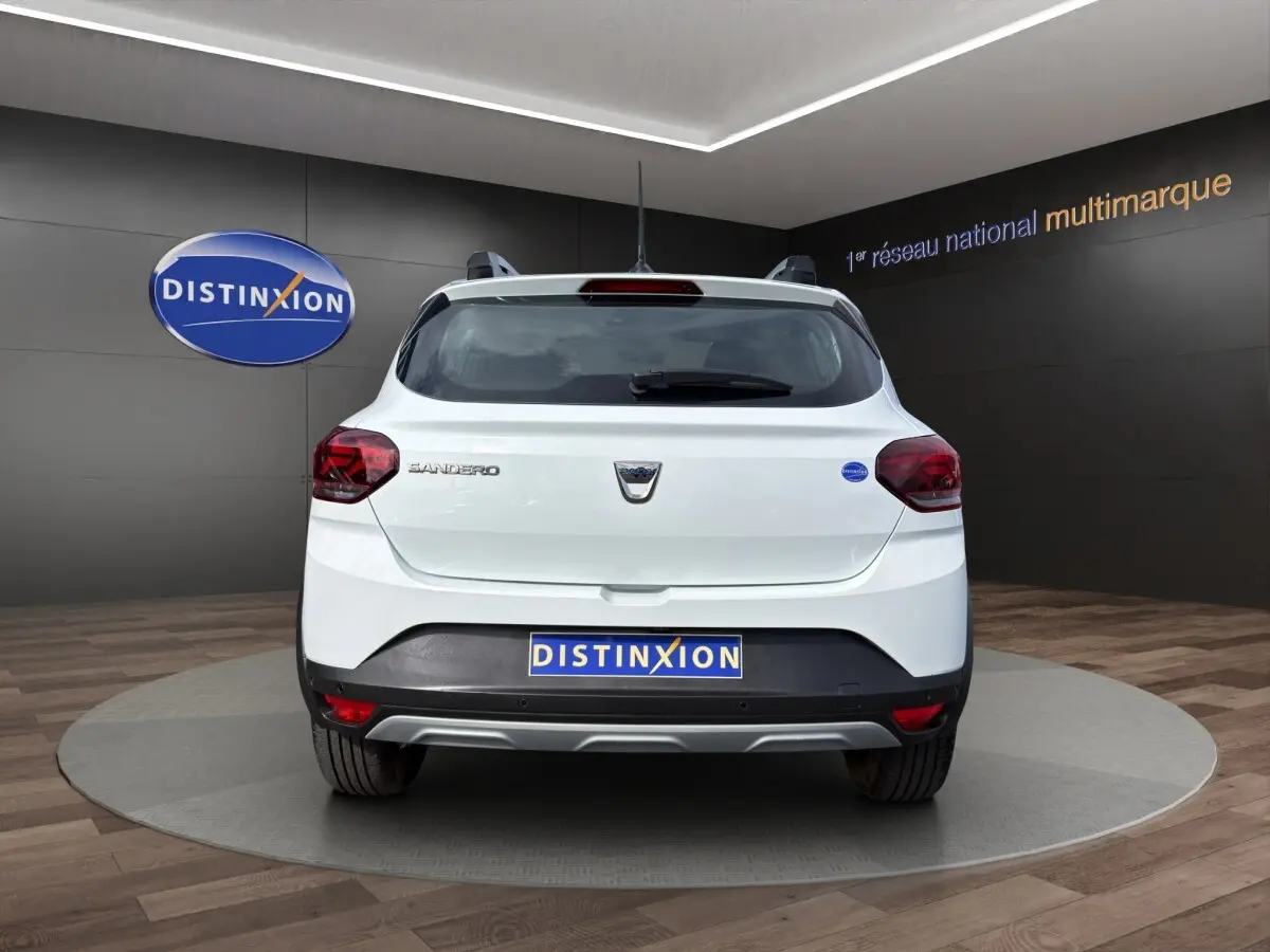 Vue arrière d'une Dacia Sandero Stepway blanche 2022, avec logo et feux arrière rouges visibles en intérieur showroom.