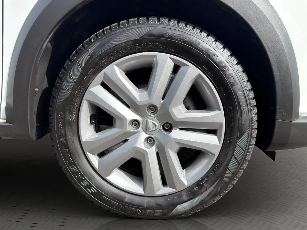 Gros plan sur la roue avant droite d'une Dacia Sandero Stepway blanche, jante alliage grise au design moderne.