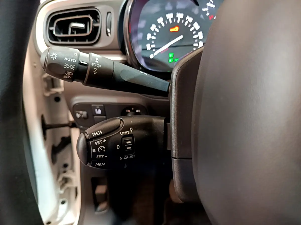 Gros plan sur les commandes au volant côté gauche de la Citroën C3 blanche, avec tableau de bord éclairé en arrière-plan.