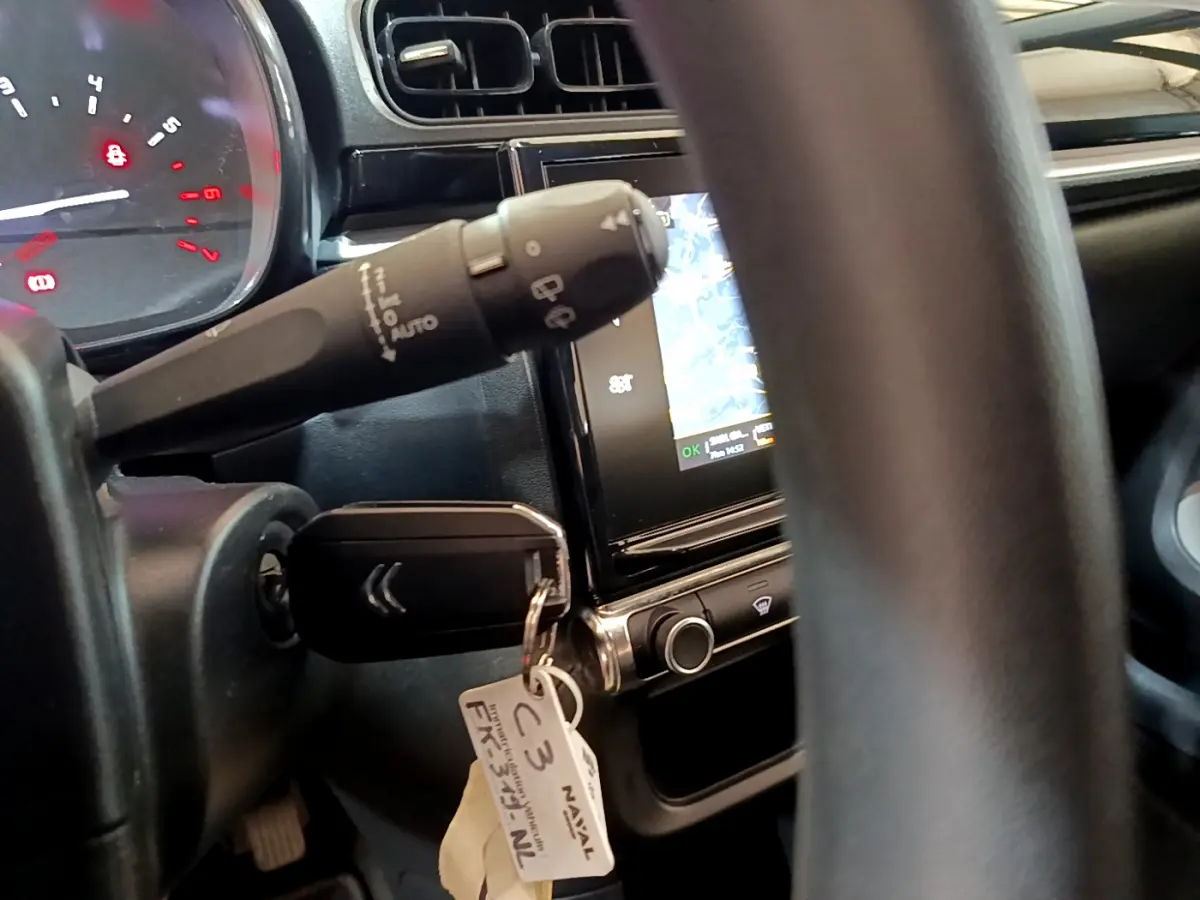 Gros plan intérieur sur le volant et la clé de contact d'une Citroën C3 blanche, avec écran tactile de navigation visible.