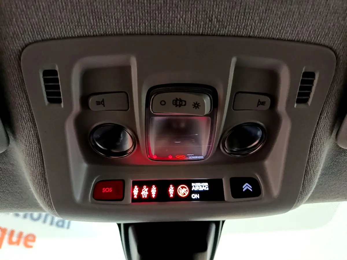 Vue en contre-plongée du plafonnier gris avec commandes d’éclairage et indicateurs lumineux allumés dans une Citroën C3 blanche.