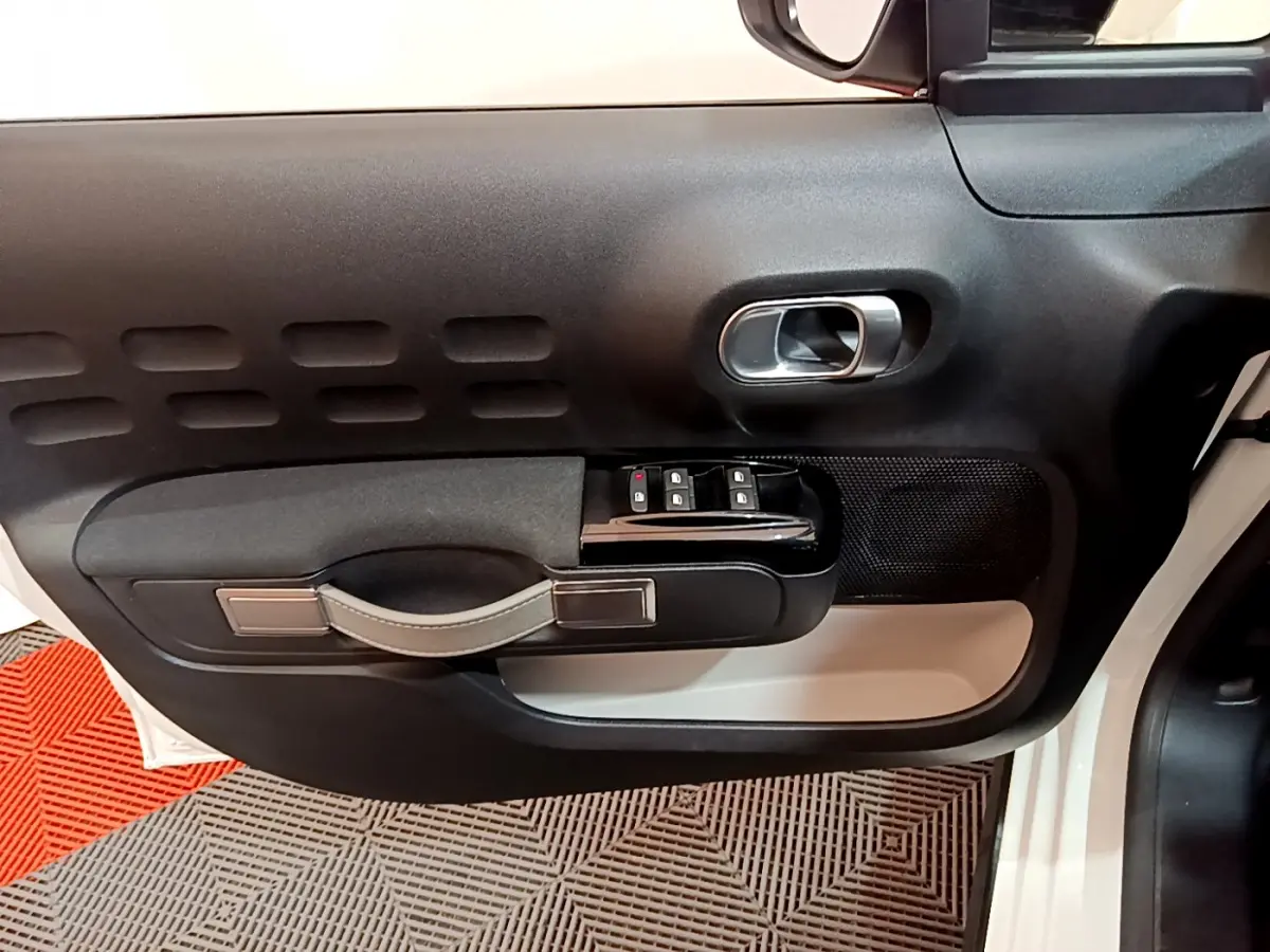 Intérieur côté gauche de la porte d'une Citroën C3 blanche 2019, avec commandes de vitres et poignée noire.