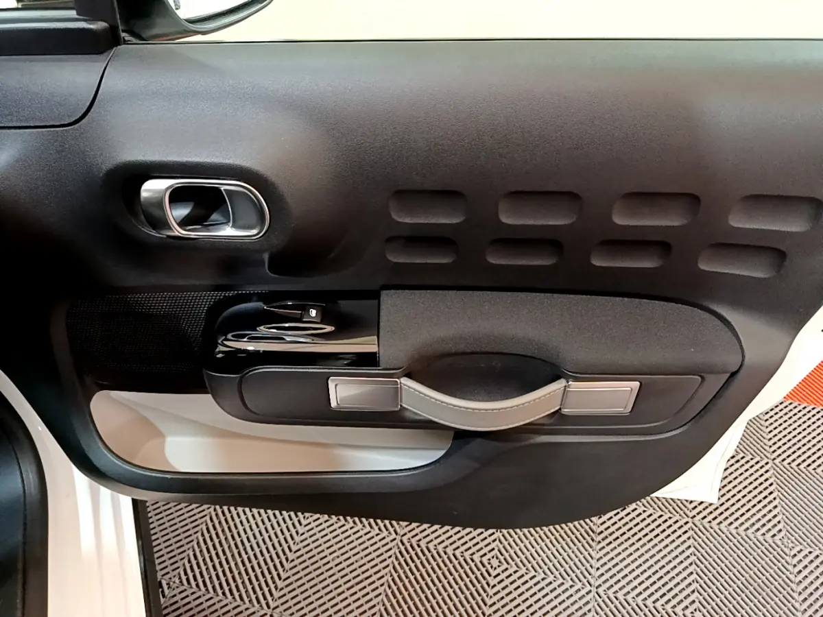 Détail de la porte côté gauche noire avec poignée en cuir et commandes de vitre d'une Citroën C3 blanche 2019.